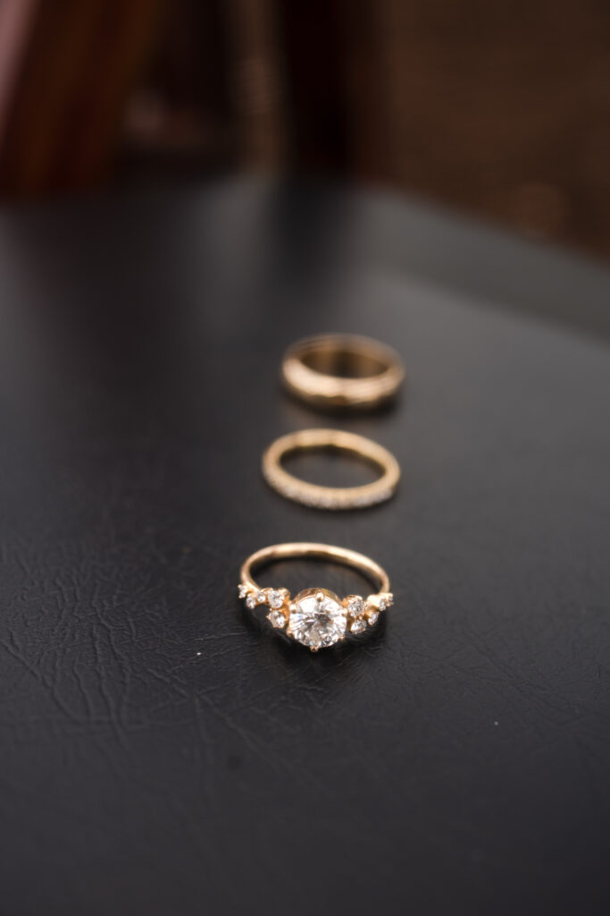 3 rings: a thick gold band, a thin gold band, and a diamond engagement ring with a gold band. 