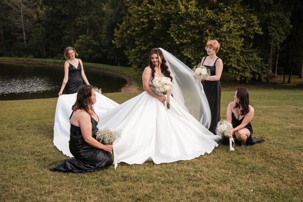 A bride in a white ballgown having her veil and dress adjusted by her four bridesmaids in black gowns. 